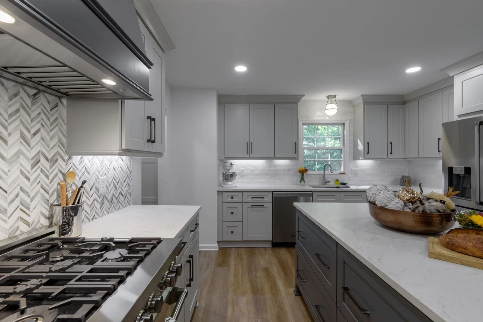Modern kitchen with gray cabinets, white countertops, stainless steel appliances, and herringbone backsplash.