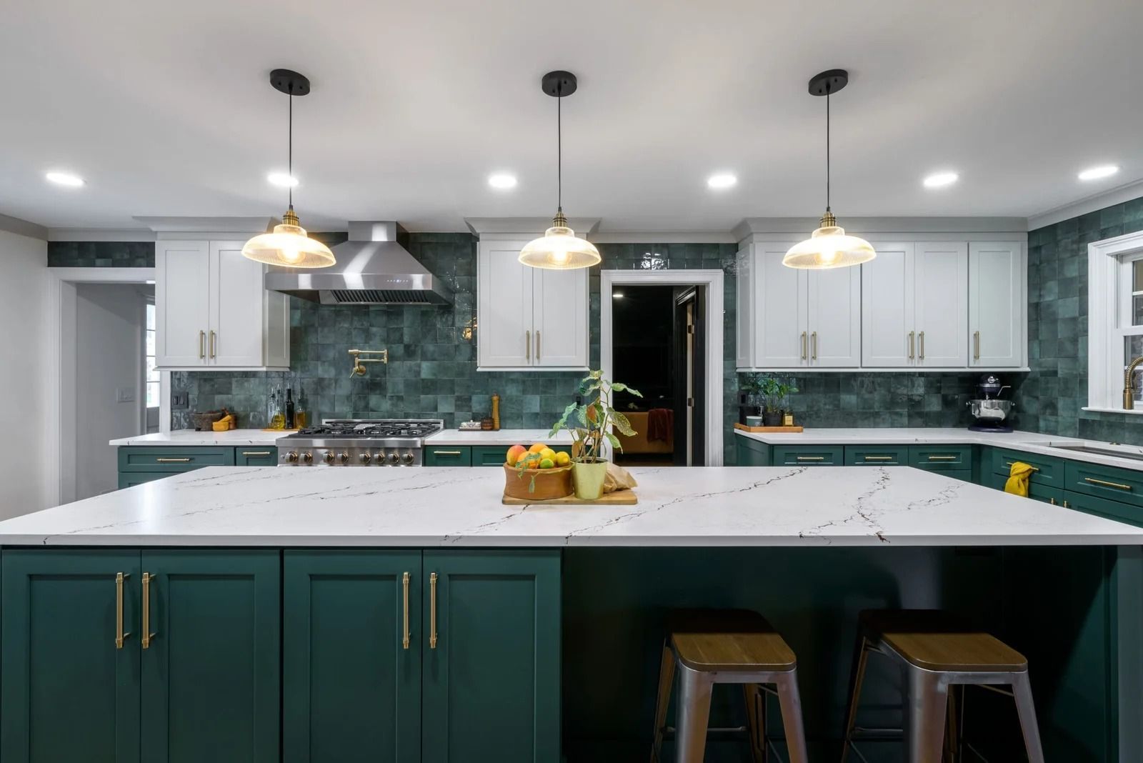 Green and white kitchen with large island, pendant lights, and teal backsplash.