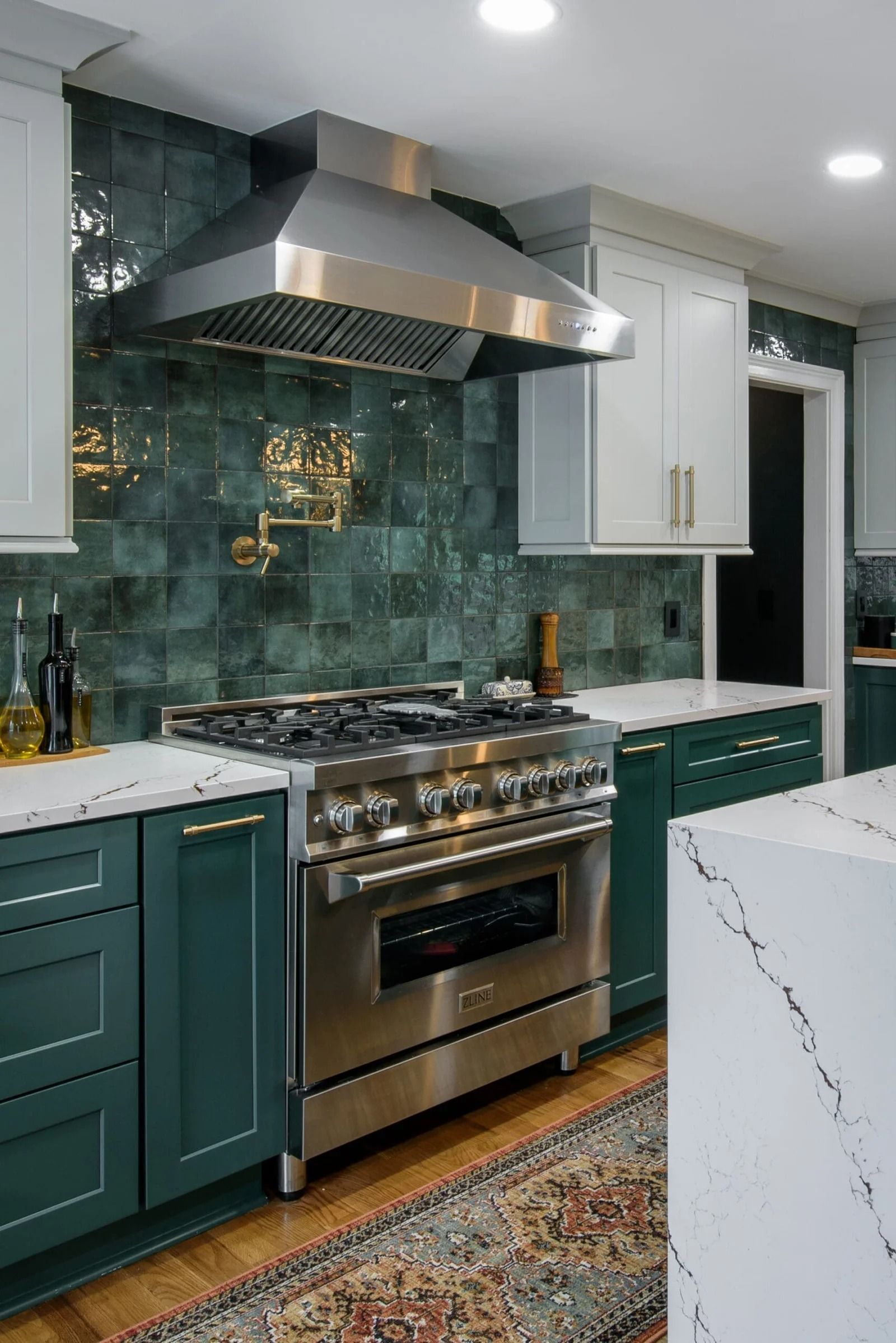 Green and white kitchen with stainless steel stove and range hood. Green tile backsplash, white countertops, and cabinets.