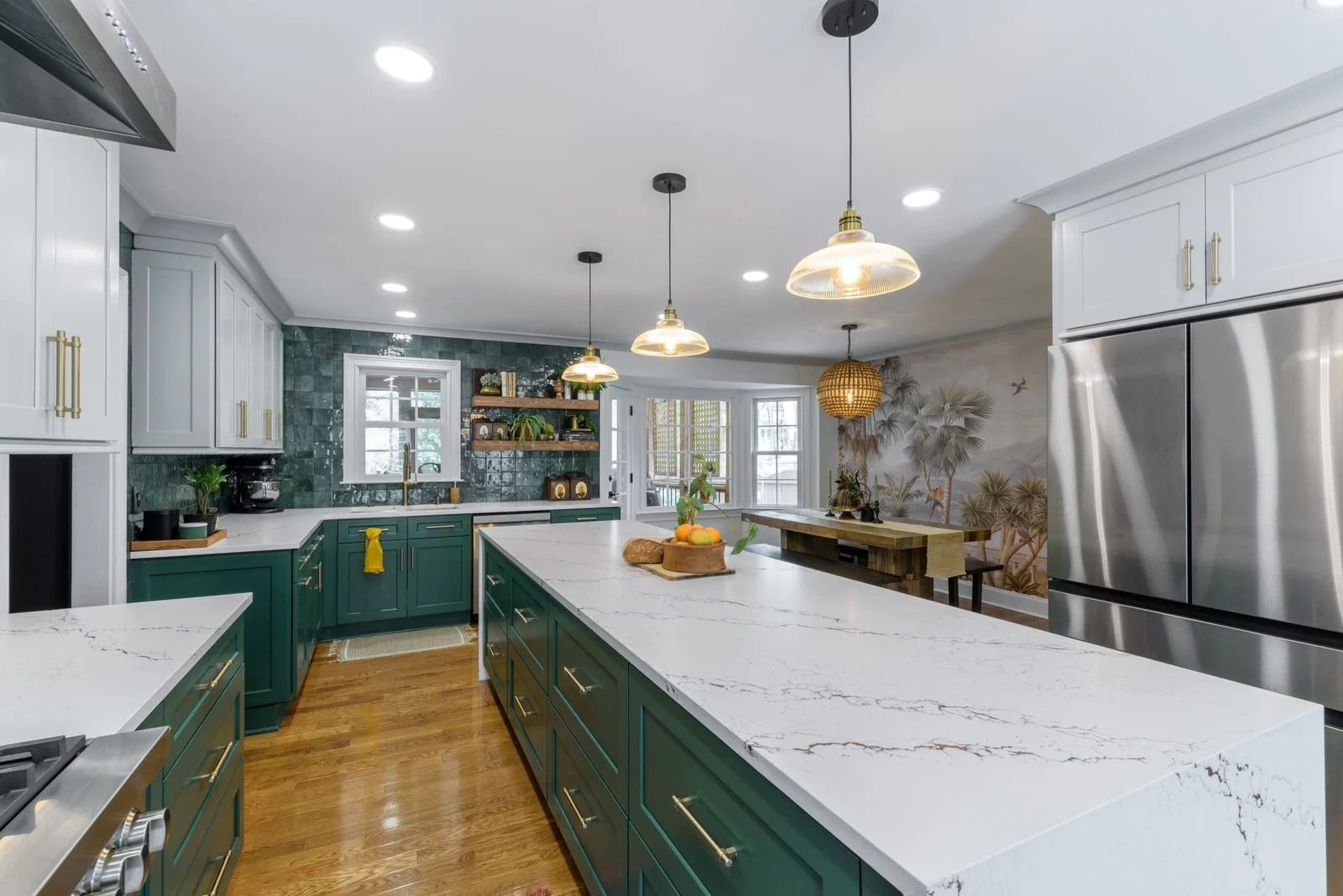 Green and white kitchen with large island, pendant lights, and stainless steel appliances.