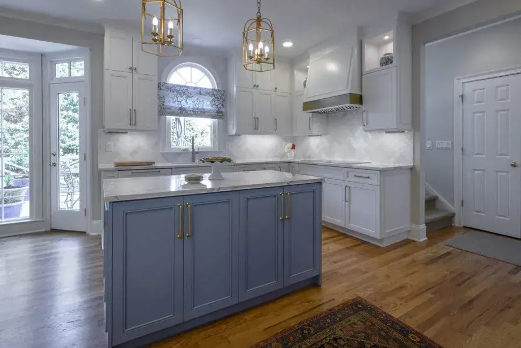 Kitchen with blue island, white cabinets, gold light fixtures, and hardwood floors.
