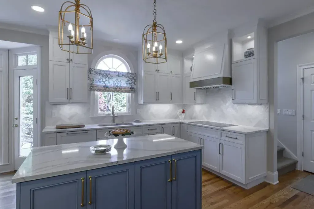 Elegant white and blue kitchen with island, pendant lights, and window.