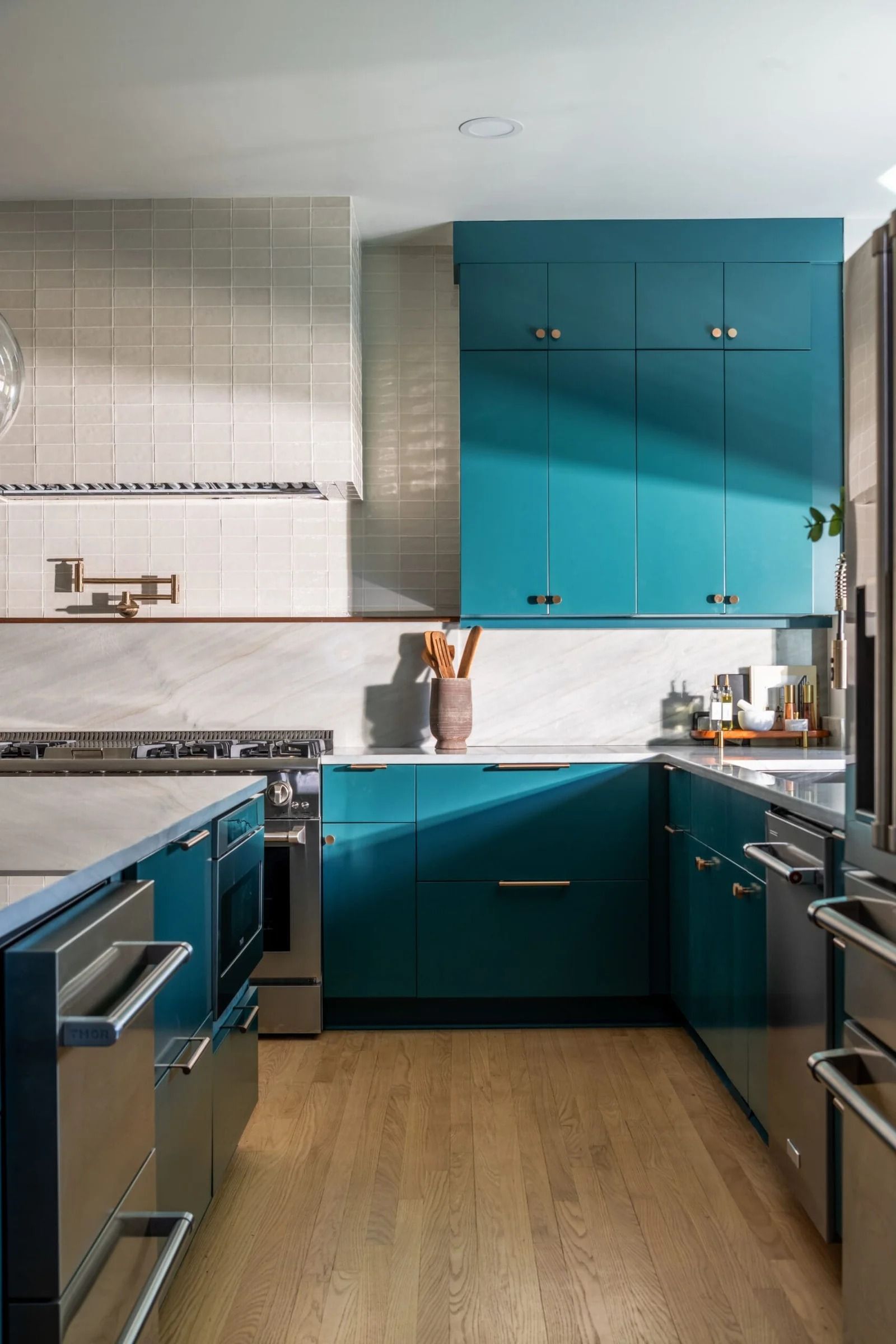 Modern kitchen with teal cabinets, stainless steel appliances, and wood flooring.
