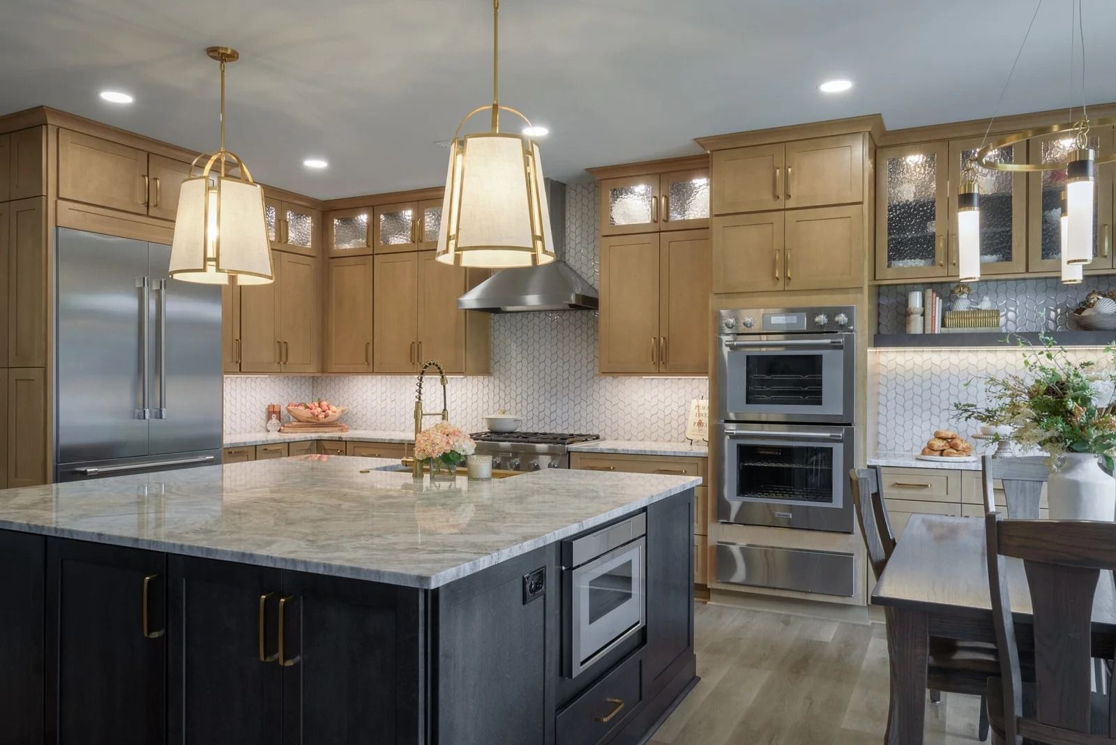 Modern kitchen with light wood cabinets, dark island, stainless steel appliances, and pendant lights.