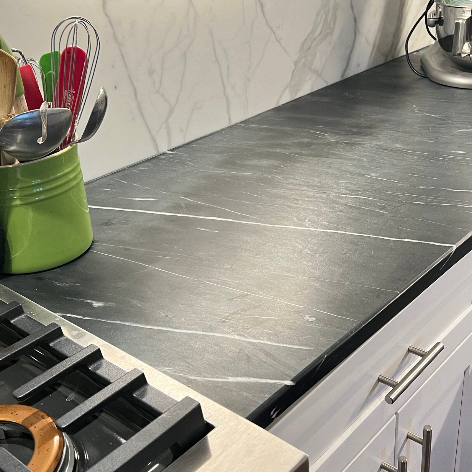 Black kitchen countertop with white veining; green utensil holder; white cabinets.