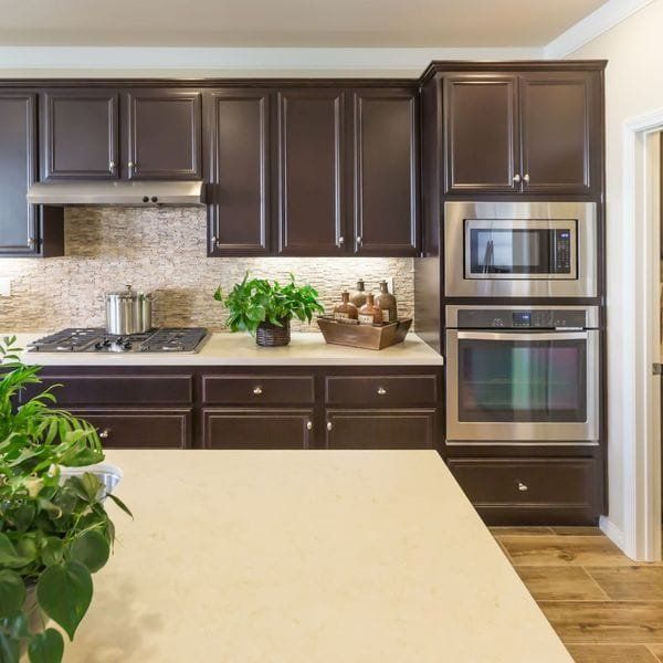 Dark brown kitchen cabinets with a microwave and oven, beige countertops, and a light-colored backsplash.