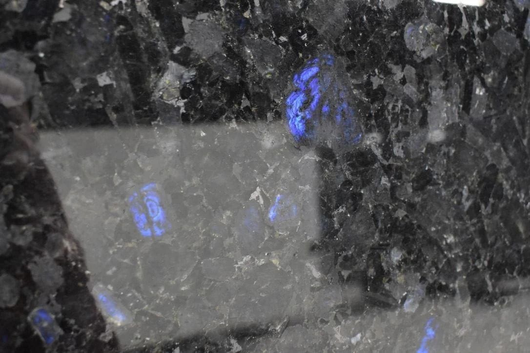 Close-up of a black granite surface with iridescent blue flashes, reflecting light.