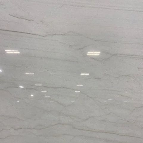 Close-up of a polished white marble surface with light brown veining and reflections.