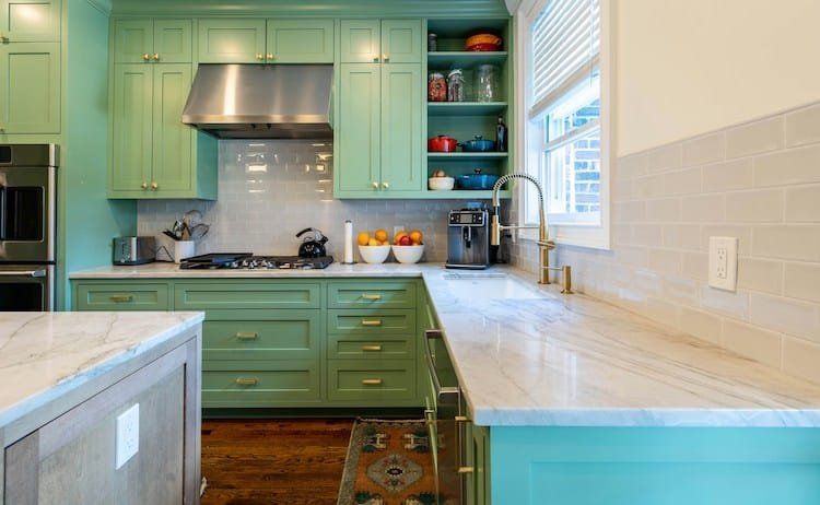 Green kitchen with white countertops and stainless steel appliances.