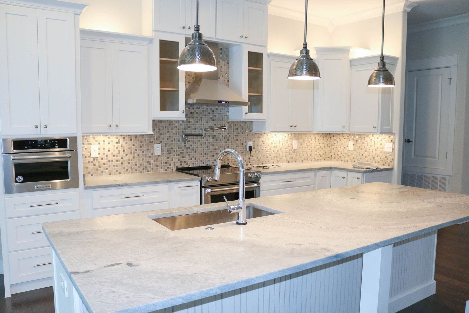 White kitchen with granite countertops, stainless steel appliances, and pendant lights.