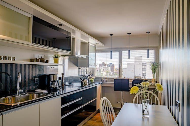 Modern kitchen with white cabinets, dark countertops, and striped walls; dining table by a window.