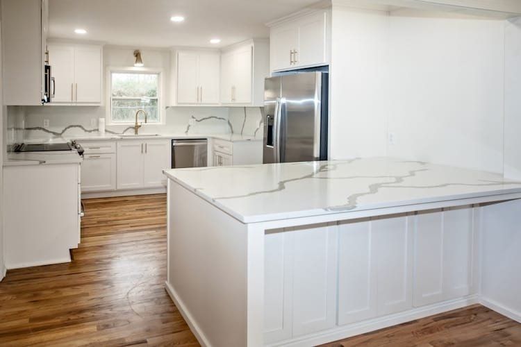 White kitchen with island, marble countertops, stainless steel appliances, and wood flooring.