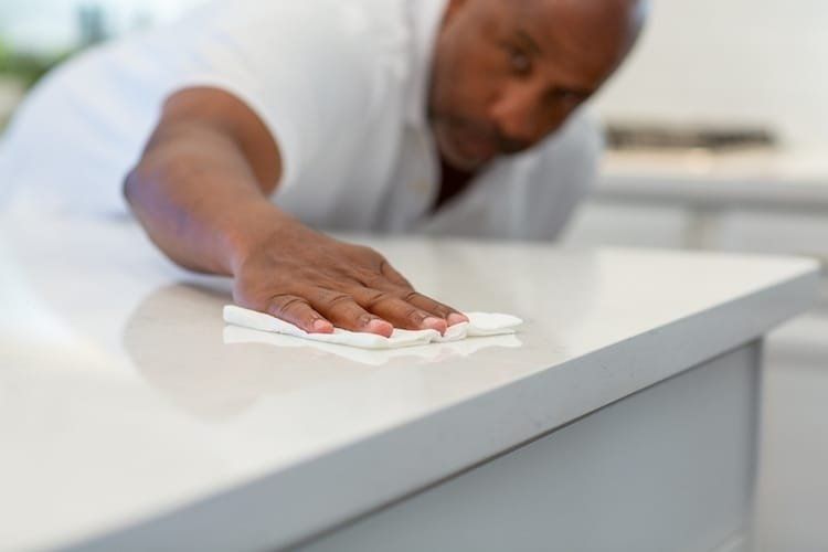 Person cleaning a white countertop with a white cloth in a kitchen.