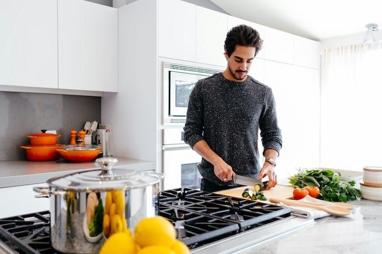 Man cutting vegetables in a bright kitchen with stove and cookware.