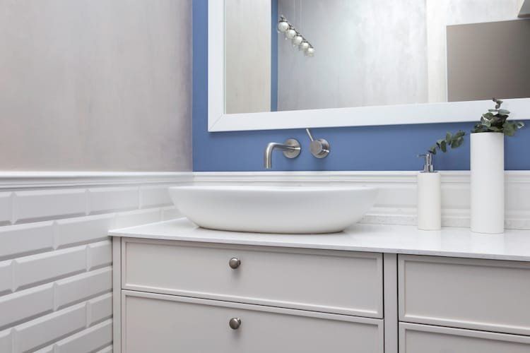 White bathroom vanity with oval sink, blue wall, white molding, and silver faucet.