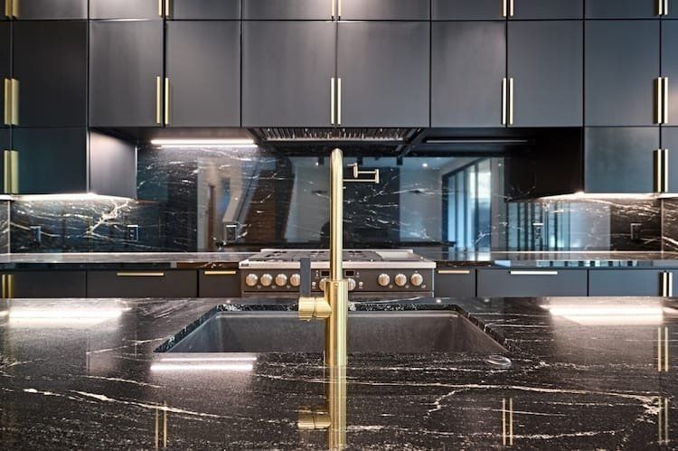 Black and gold luxury kitchen with marble backsplash and countertops; gold fixtures, range and cabinets.
