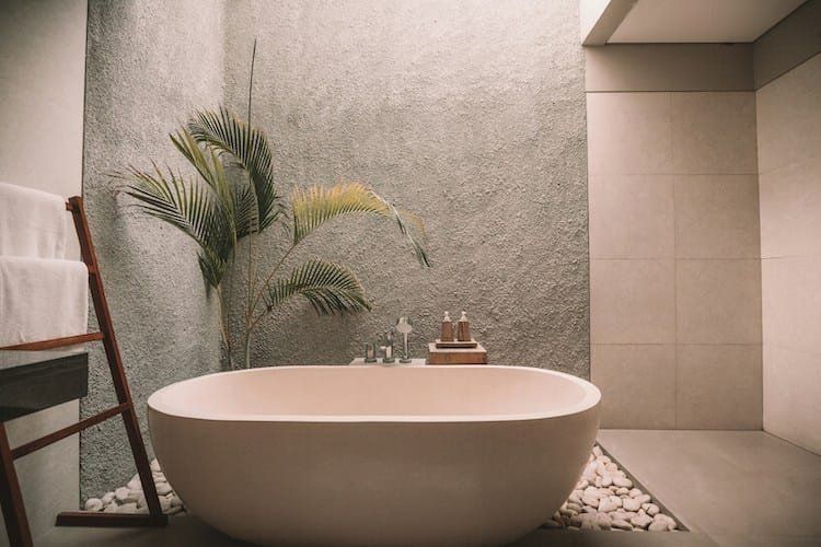 Minimalist bathroom with a white oval bathtub, plants, and pebble accents.