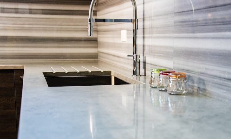 Modern kitchen sink with marble countertop and backsplash, glass jars on the right.