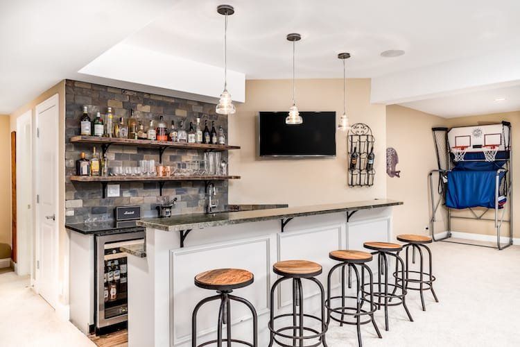 Basement bar with stone accent wall, wooden shelves, stools, TV, and basketball hoop.