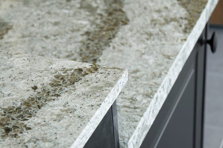 Close-up of a granite countertop with a light, speckled pattern. The edge is squared off, with dark cabinets.
