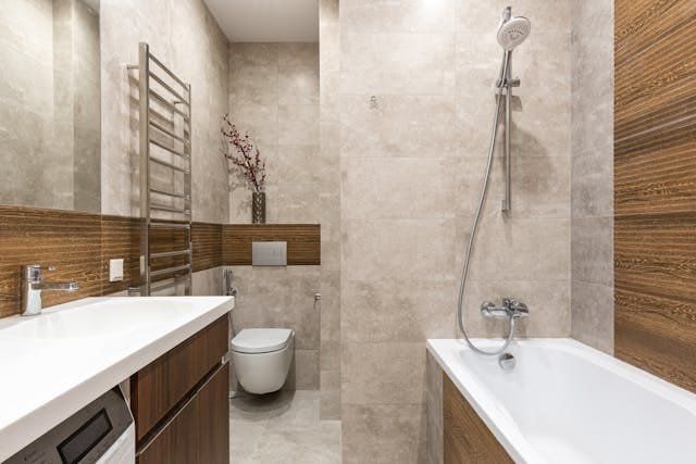 Bathroom with beige tile walls, wood accents, white sink, toilet, bathtub, and silver towel rack.