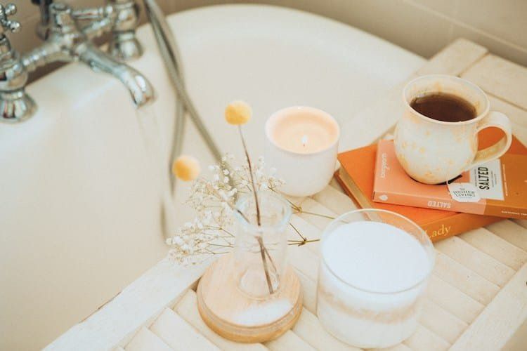 Bathtub scene with tea, candle, flowers, and books on a wooden tray.