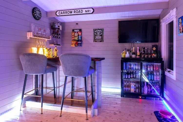 Home bar interior with bar stools, drinks, TV, and neon lighting.