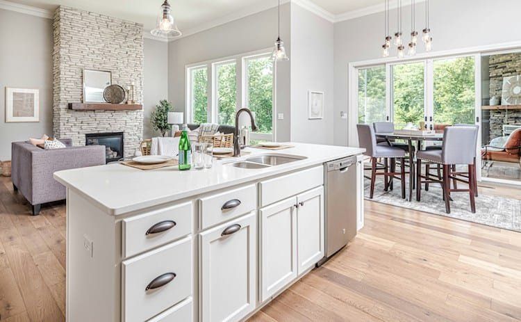 Open-concept kitchen with white island, stainless steel appliances, and wooden flooring. Living room with fireplace is visible.