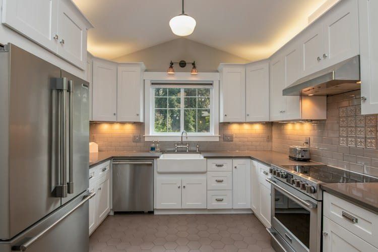 White kitchen with stainless steel appliances, cabinets, and a farmhouse sink under a window.
