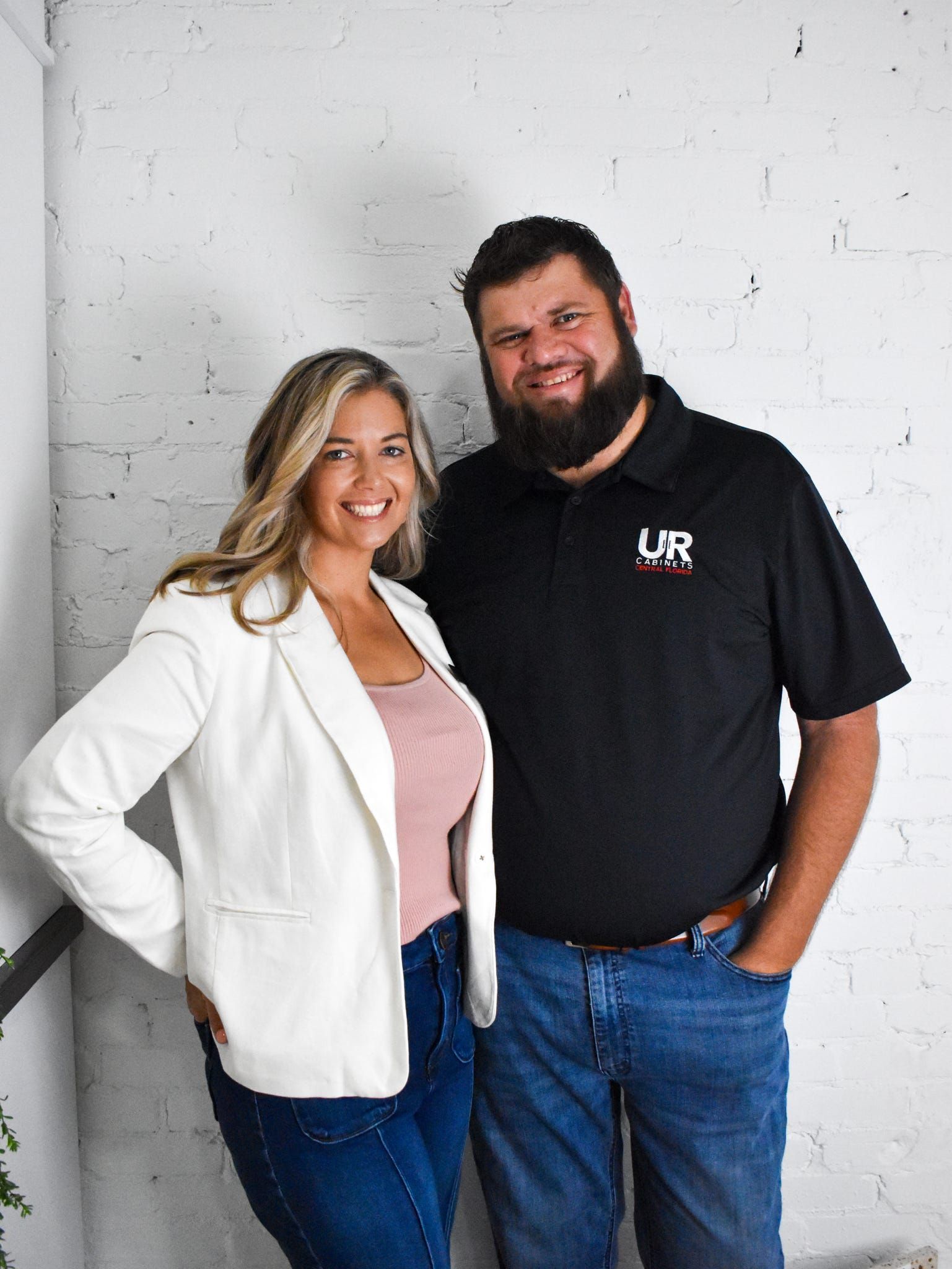 A man and a woman are standing next to each other in front of a white brick wall.