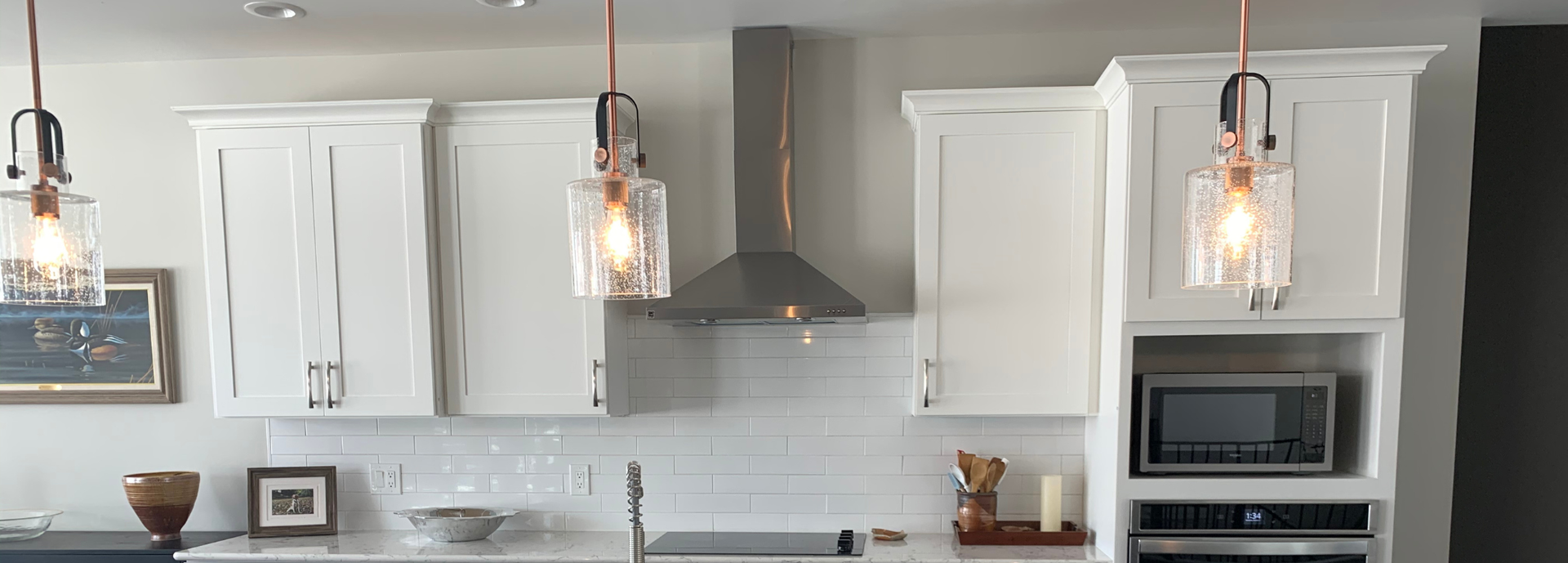 A kitchen with white cabinets and copper pendant lights.