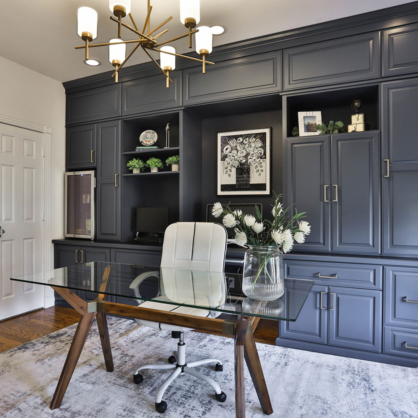 A home office with a desk , chair , cabinets and a chandelier.