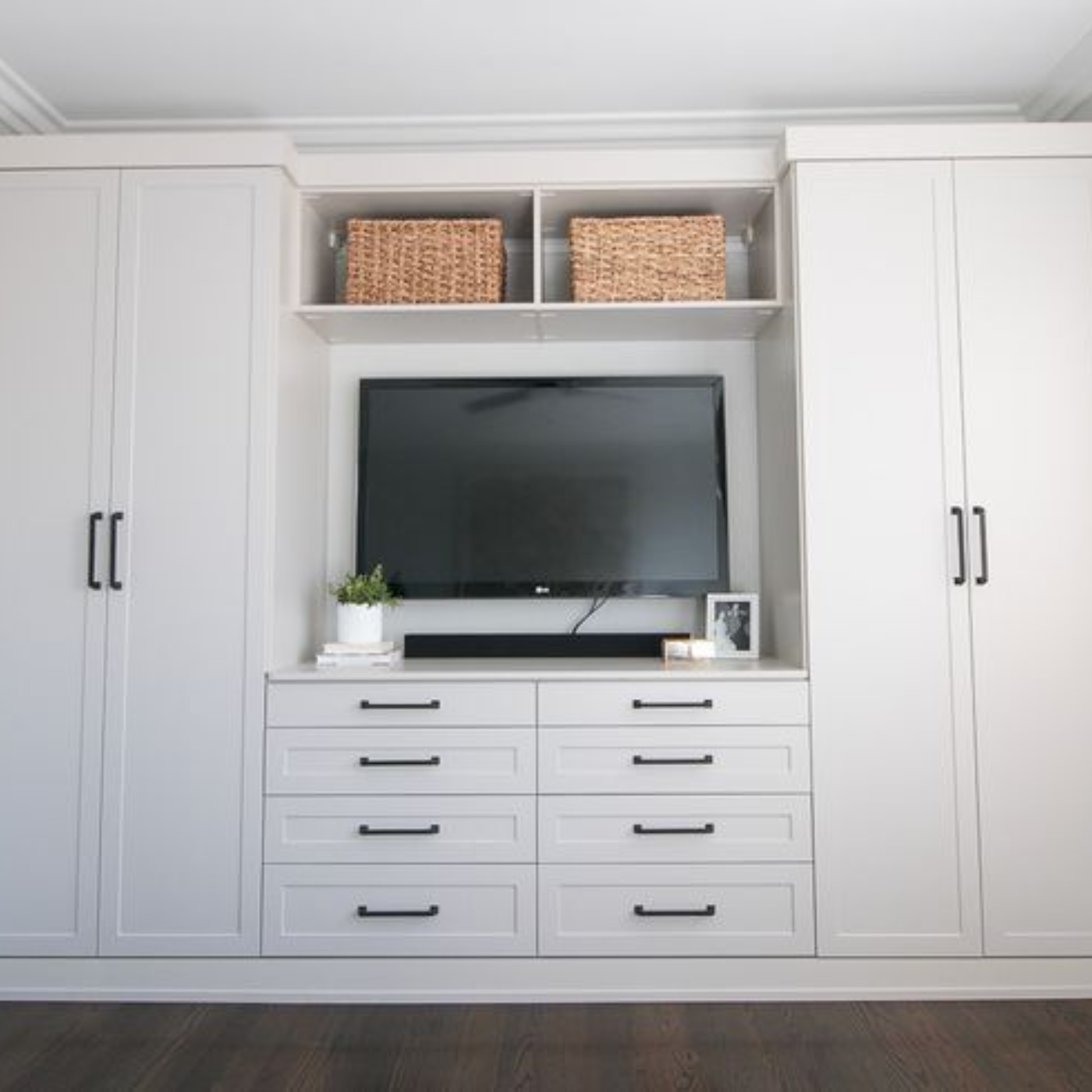 A living room with white cabinets , drawers and a flat screen tv.