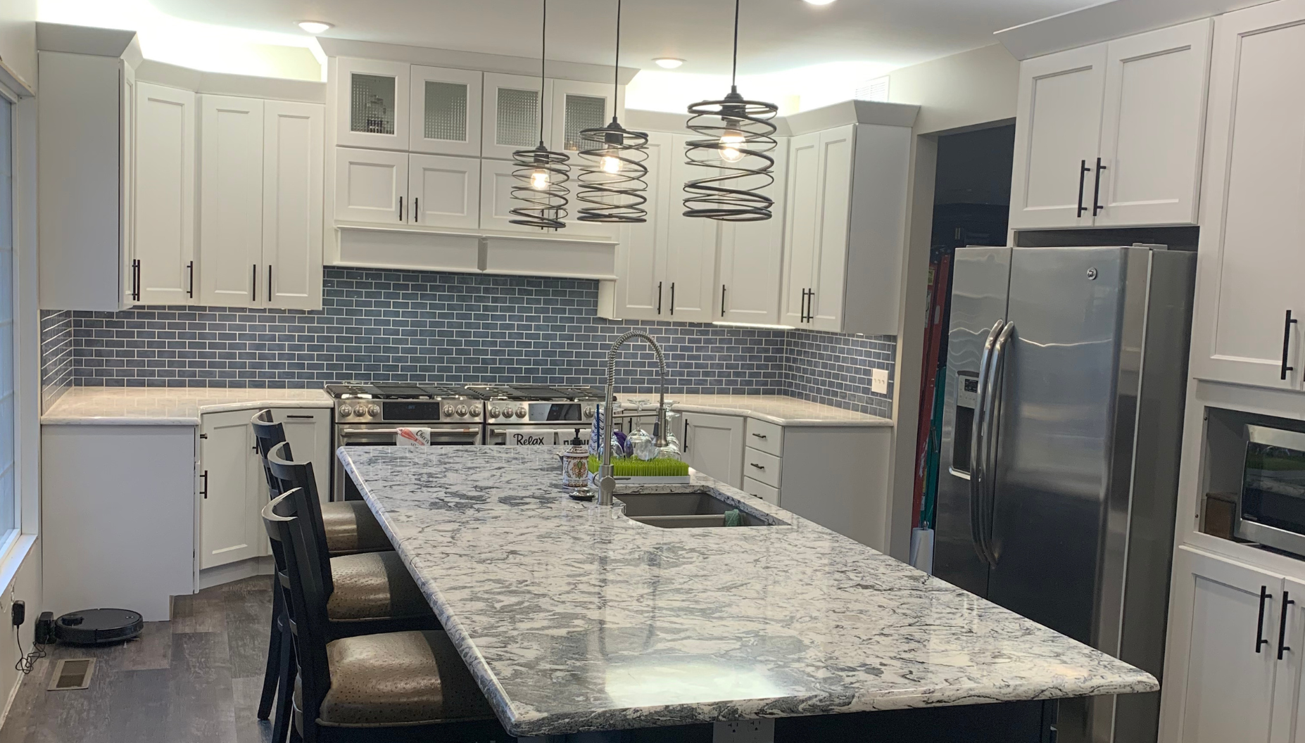 A kitchen with white cabinets , granite counter tops , stainless steel appliances and a large island.