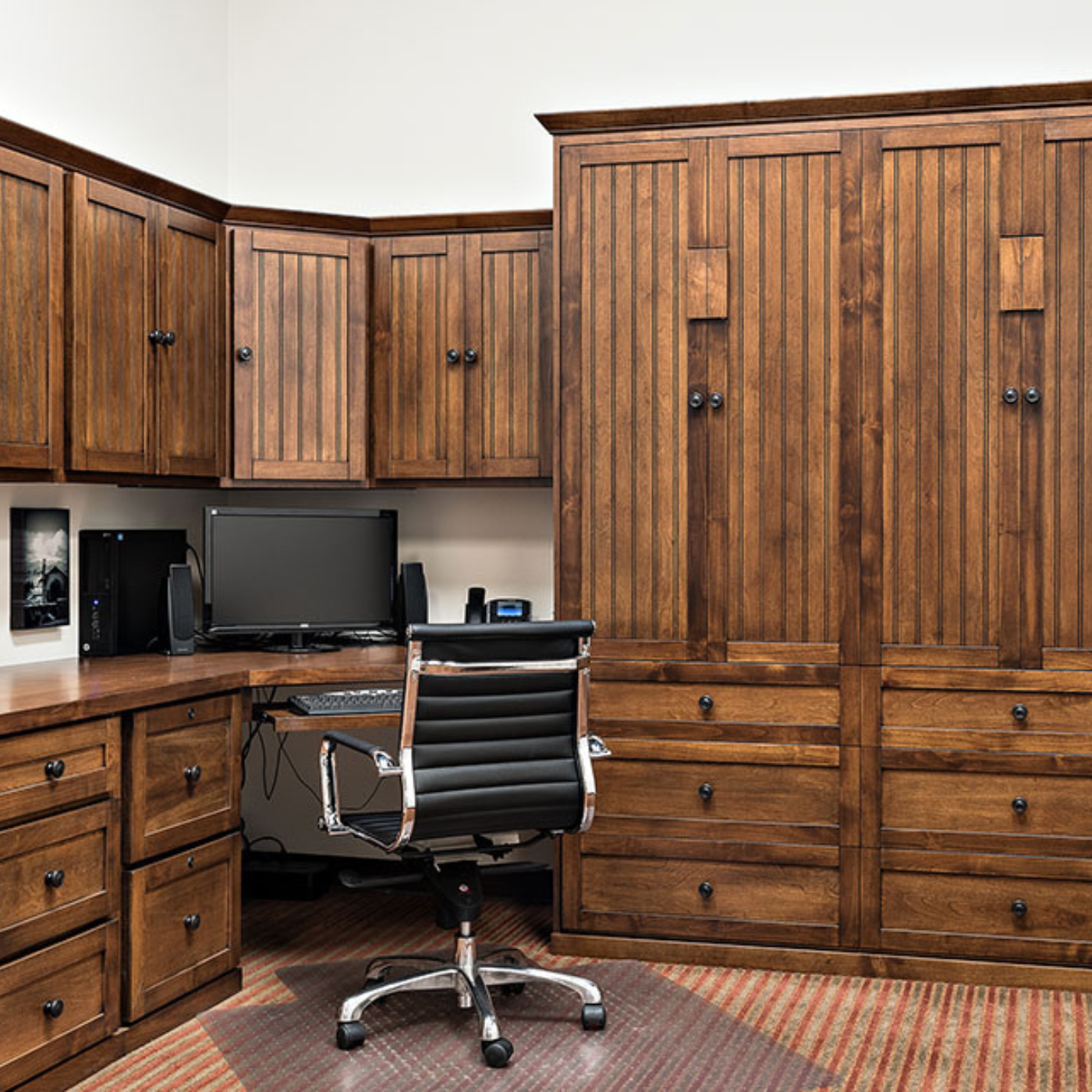 A desk with a computer and a chair in a room with wooden cabinets