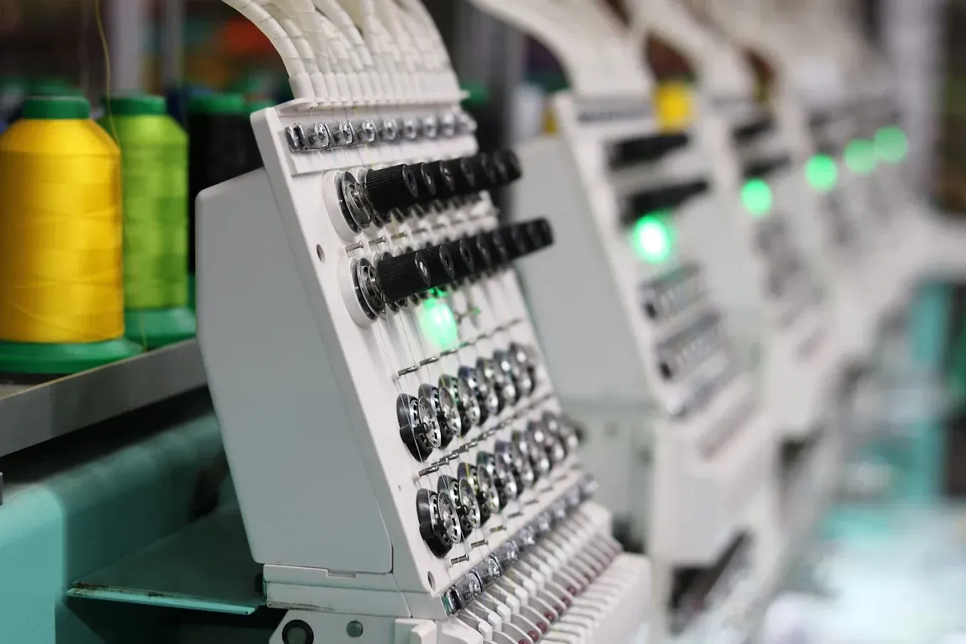Embroidery machines with spools of yellow and green thread.