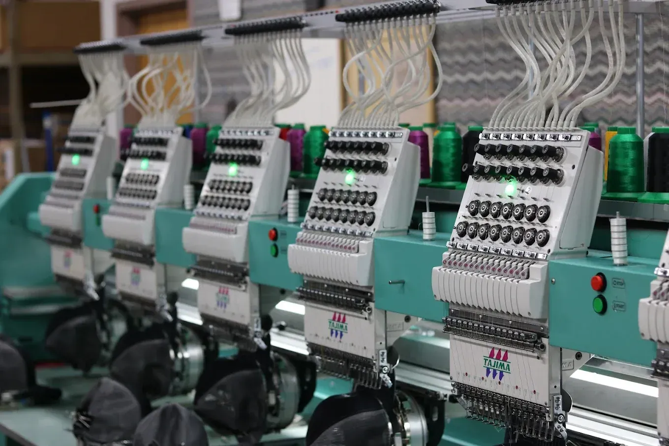 Row of industrial embroidery machines with spools of colorful thread.