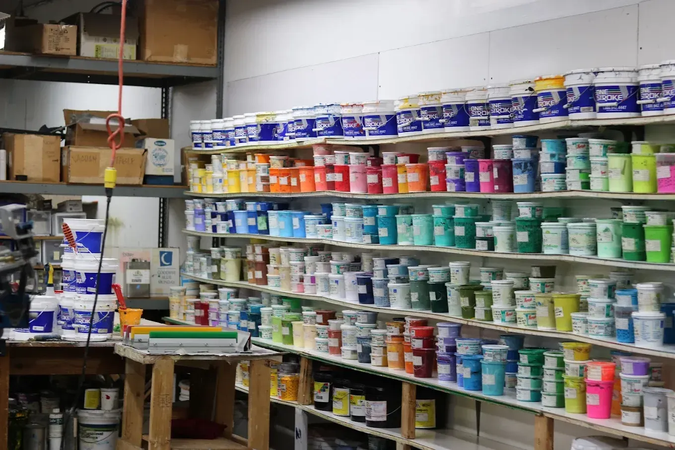 Shelves filled with colorful paint cans in a store, arranged by color, against a white wall.