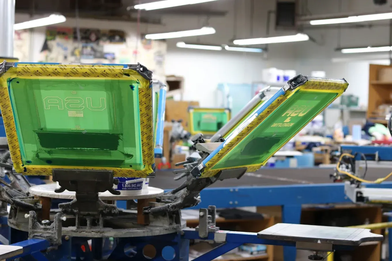 Screen printing machine in a workshop, with multiple screens, in a room with fluorescent lighting.