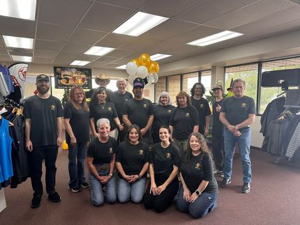 Group of people in black shirts posing indoors with balloons and merchandise.