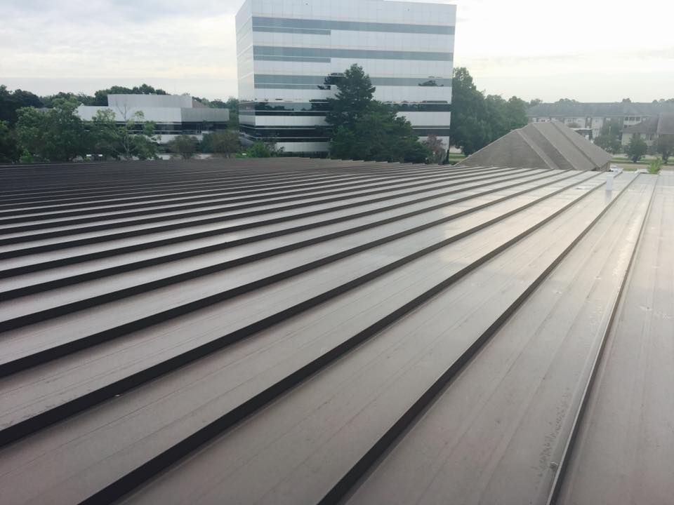Rooftop with parallel metal panels leading to a white office building under a cloudy sky