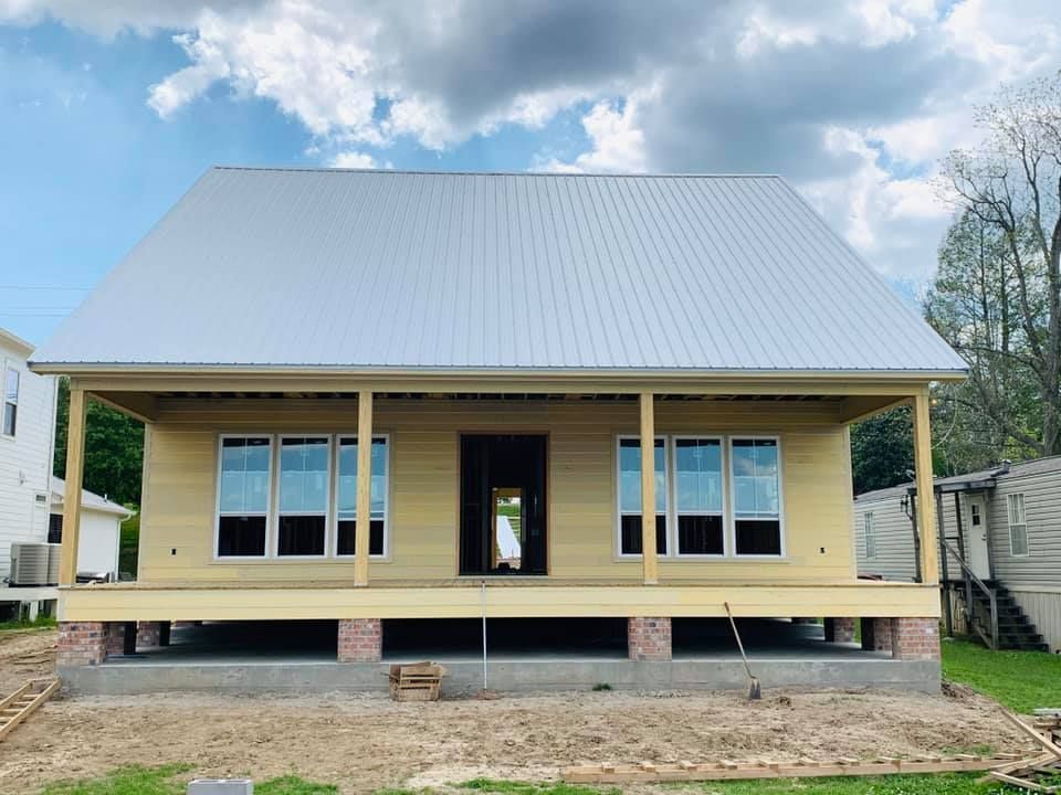 Front view of a partially finished yellow house with a metal roof and porch under a cloudy sky