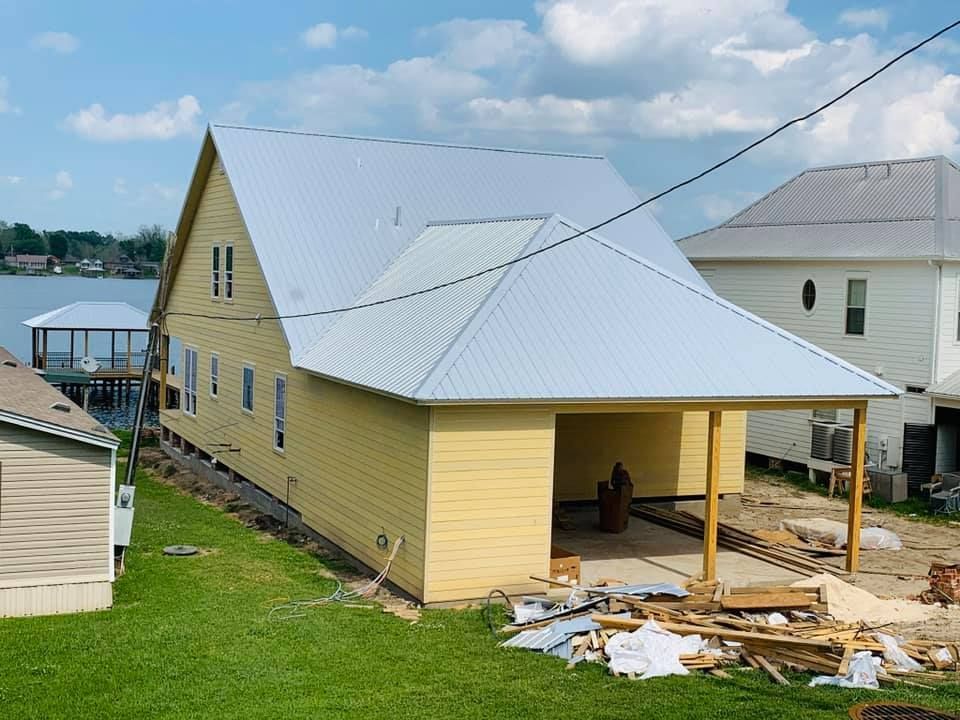 Yellow house with metal roof under construction, with debris and a porch in a residential neighborhood.