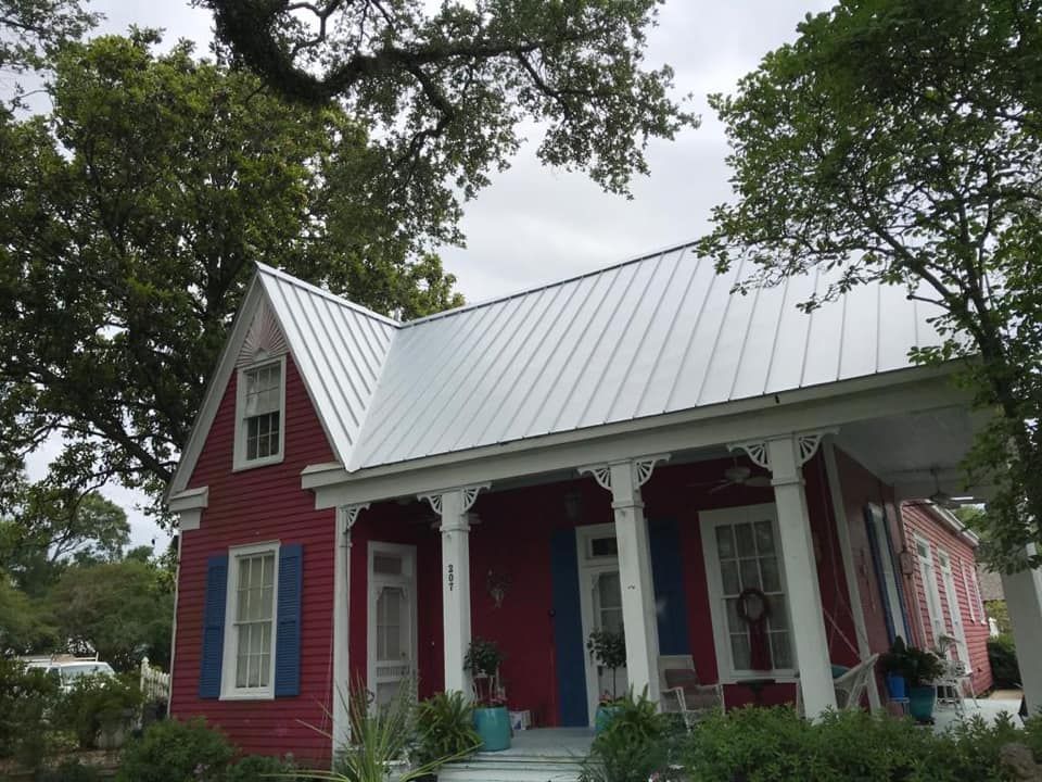 Red house with white trim and porch under tall trees on a cloudy day