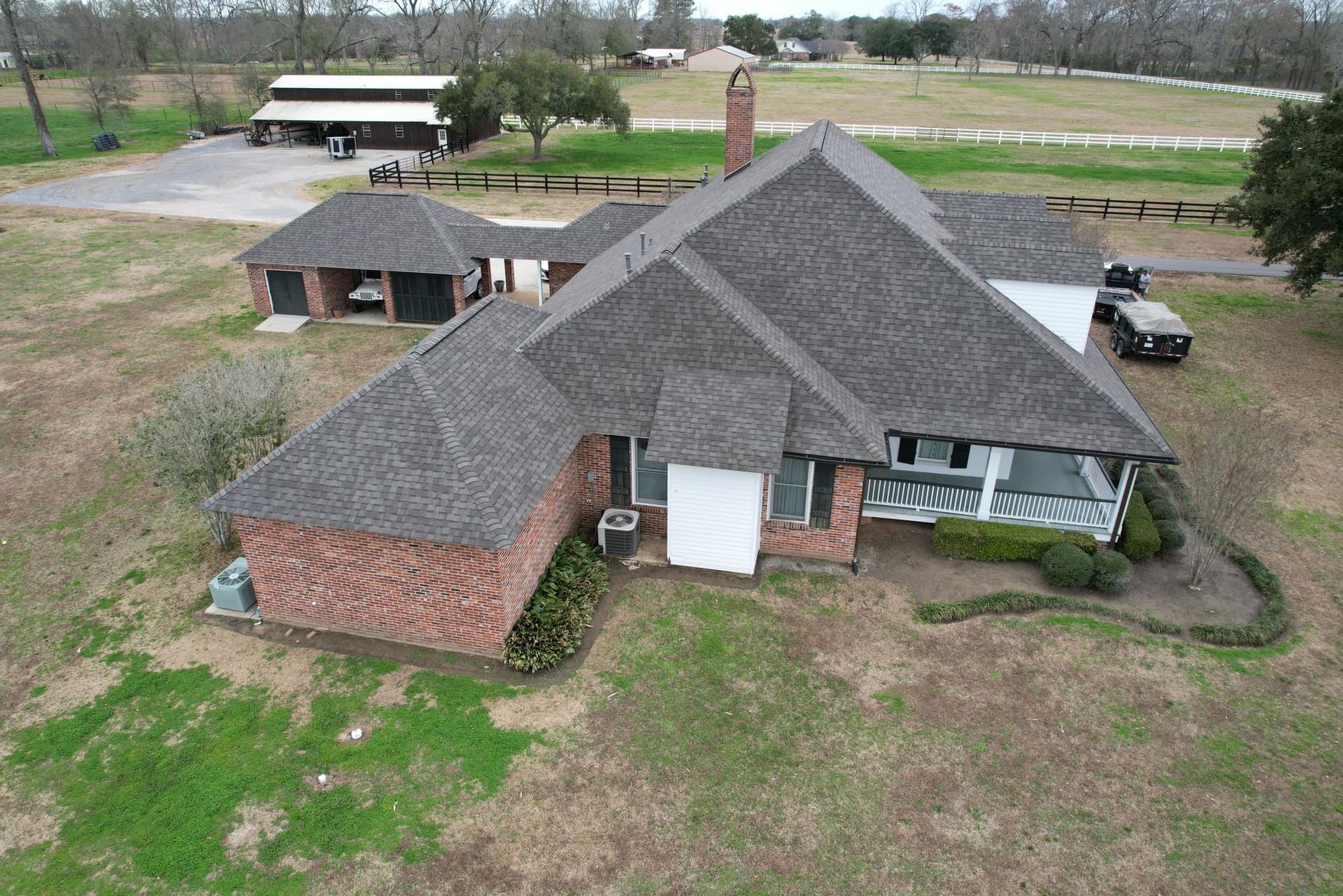 Aerial view of a large brick house with a gray roof and surrounding yard in a rural area