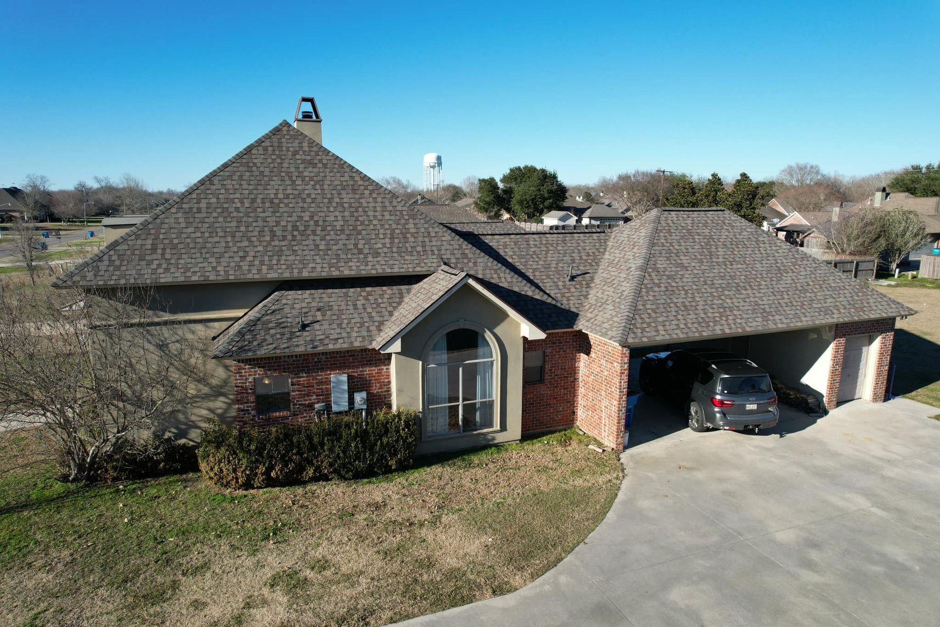 Suburban brick house with a dark shingled roof and attached garage under a clear blue sky