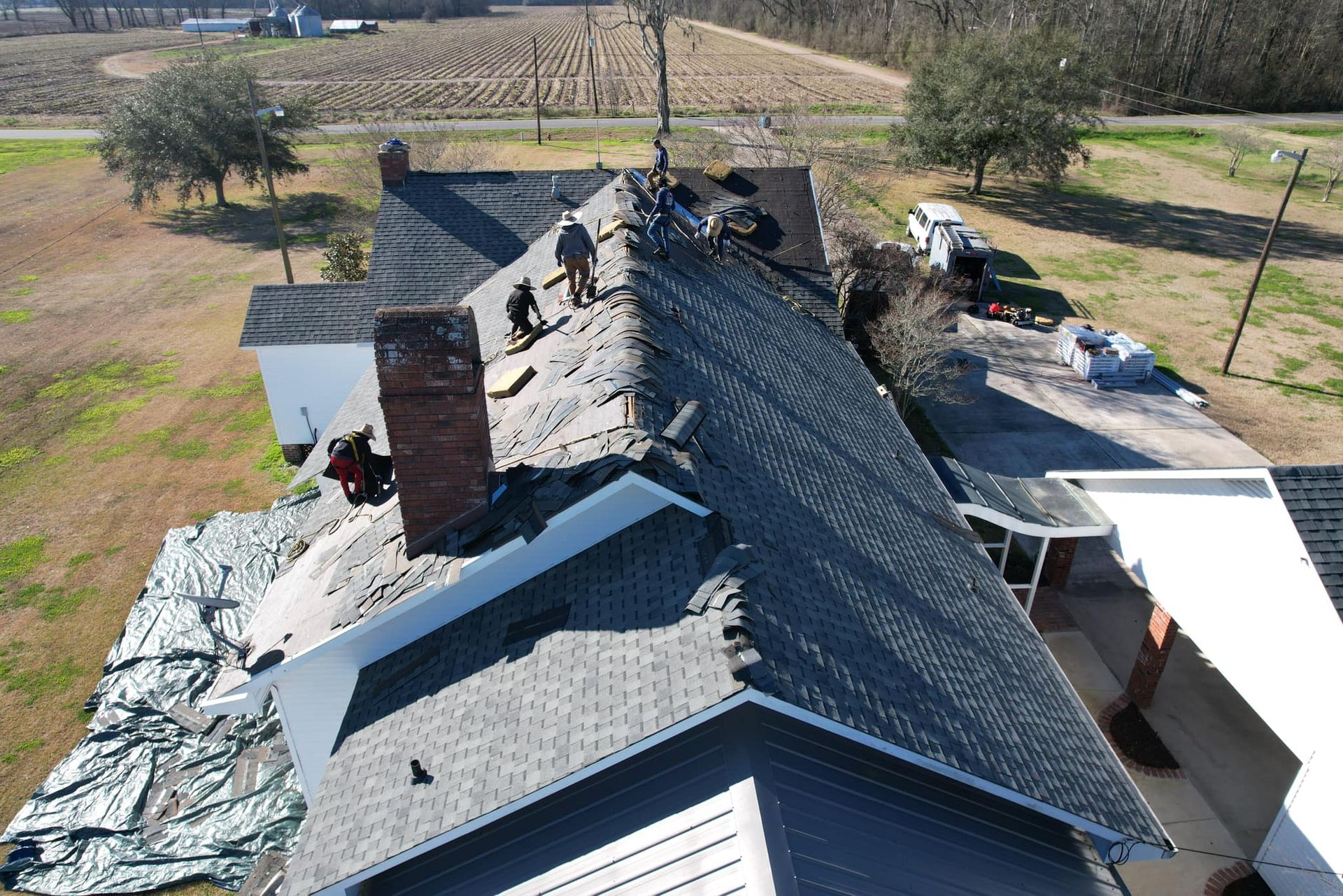 Aerial view of a house roof with workers repairing shingles and a chimney.