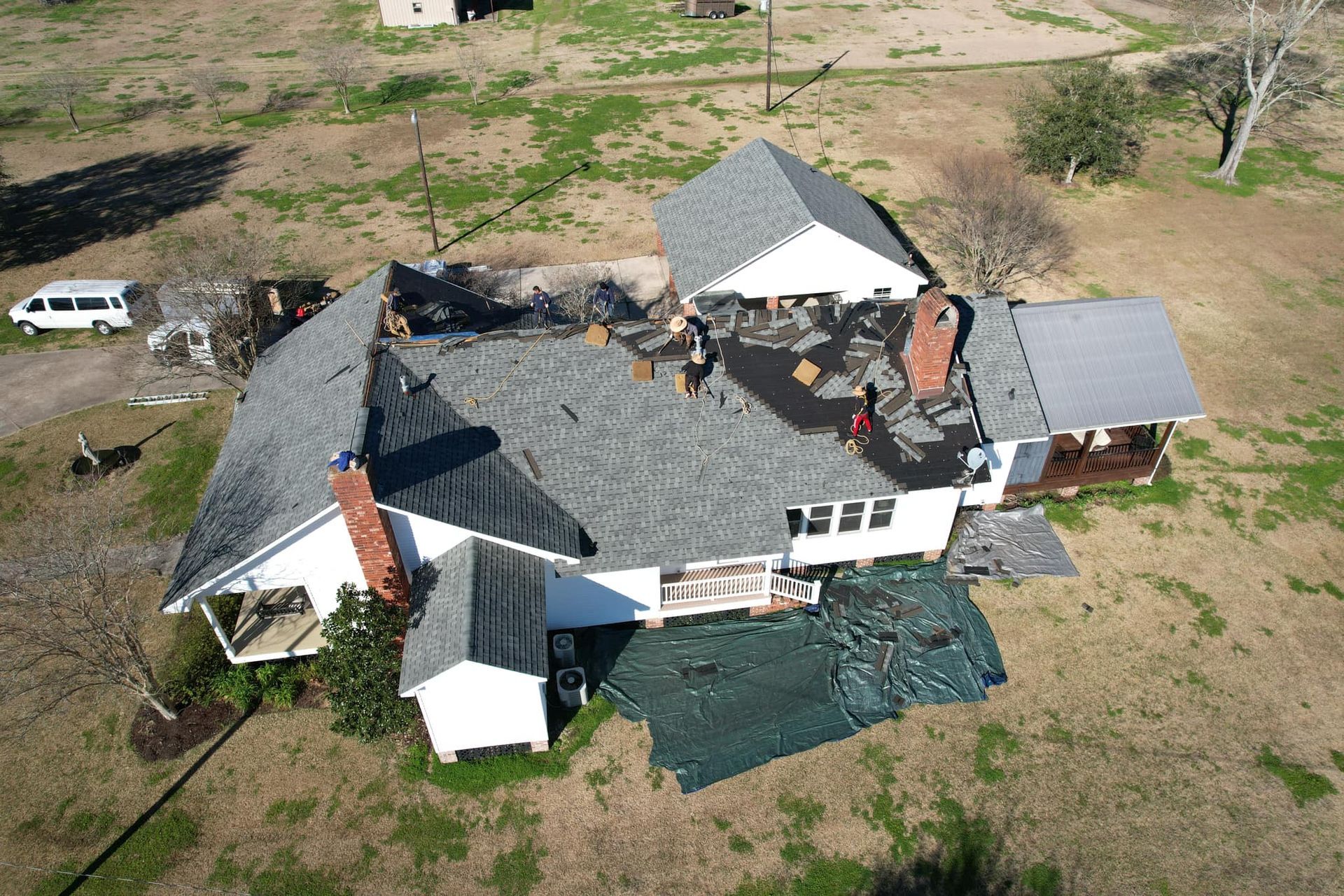 Aerial view of a partially damaged house with roof repairs in a rural area.