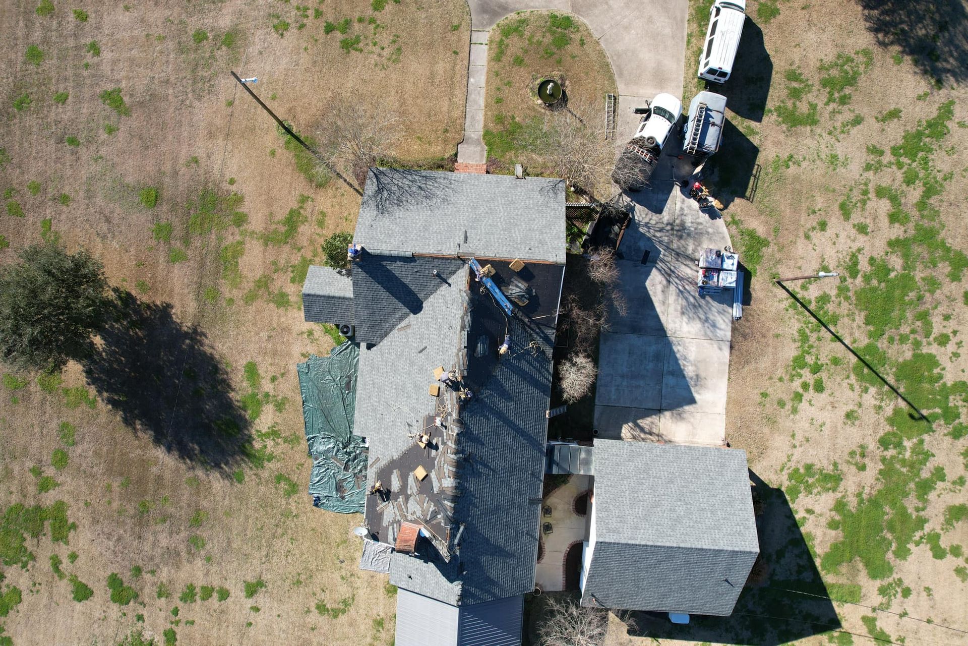Aerial view of a gray-roofed house with a small yard, driveway, and parked vehicles.