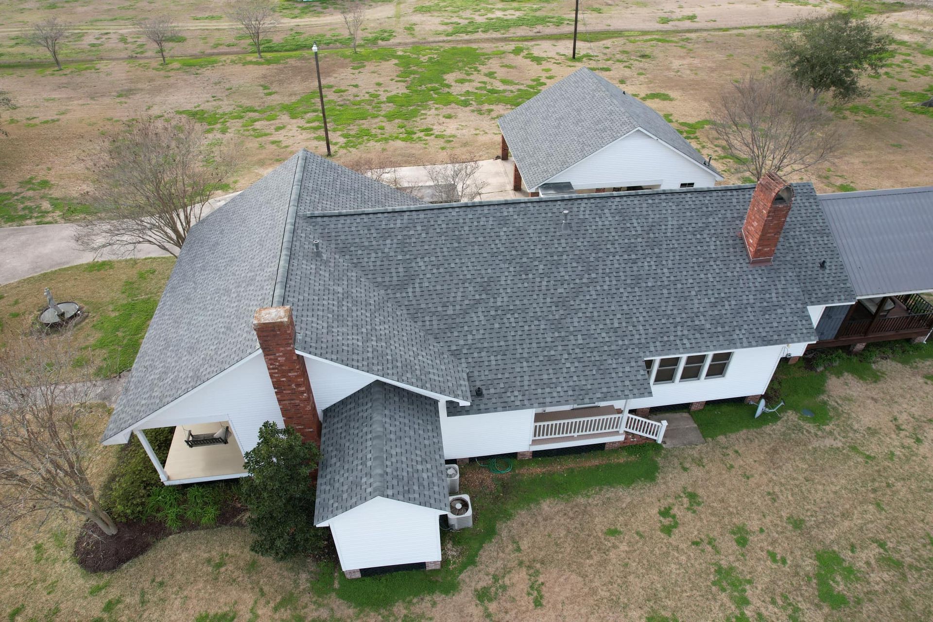 Aerial view of a white farmhouse with a gray roof and two red chimneys in a rural yard